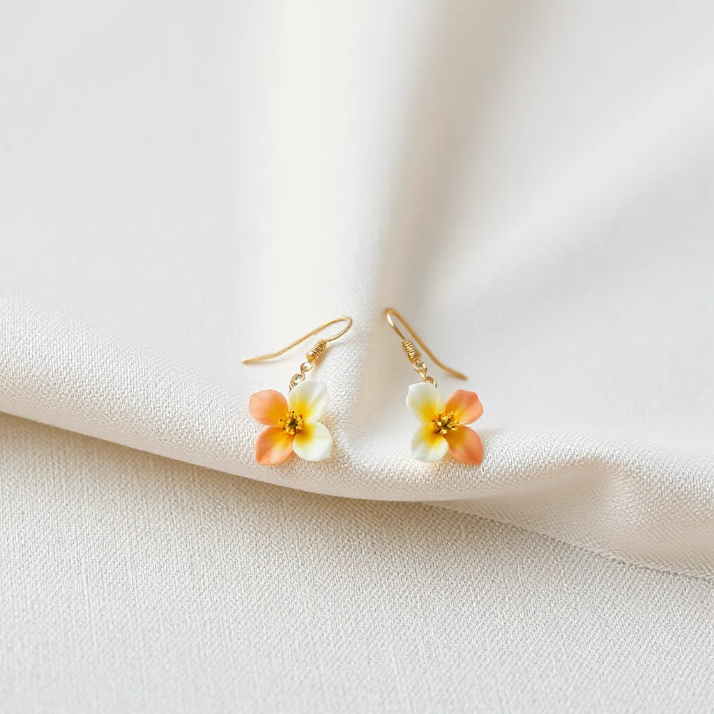 Delicate floral earrings with subtle metallic shine arranged on neutral fabric under soft natural light