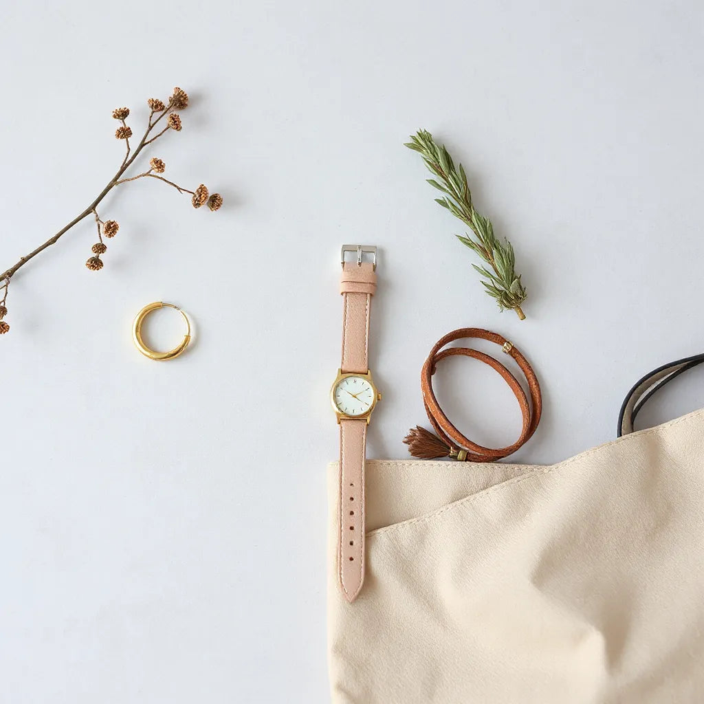 Minimalist accessories laid out on a clean surface with a watch, necklace, earrings, and bracelet