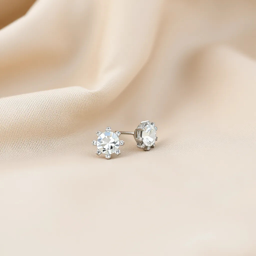 Pair of silver-toned rhinestone earrings with clear stones on neutral fabric under soft light